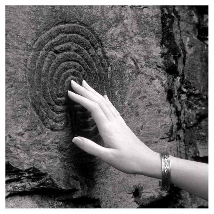 A hand resting on a spiral carved into stone